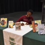 Jacqueline Woodson sitting at a table signing a book